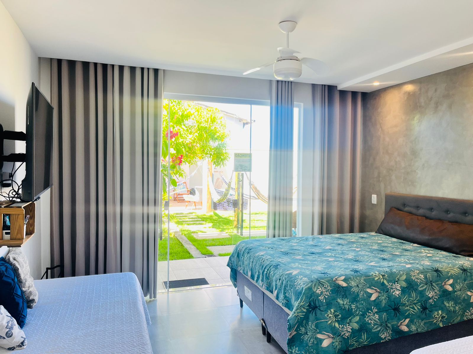 Quarto com cama de casal, cama auxiliar, TV e acesso à área externa